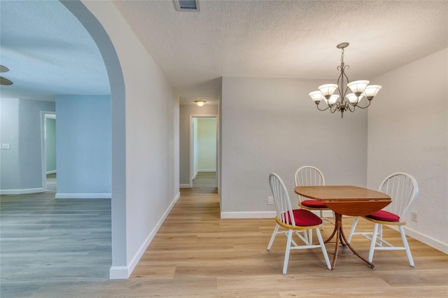 dining space with a textured ceiling, light hardwood / wood-style floors, and a chandelier