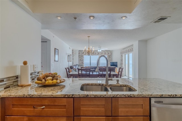 kitchen featuring sink, light stone counters, an inviting chandelier, a textured ceiling, and dishwasher