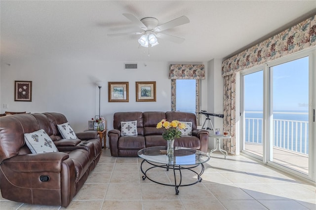 tiled living room with ceiling fan, a water view, and a textured ceiling