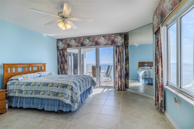 tiled bedroom with a water view, access to exterior, multiple windows, and a textured ceiling