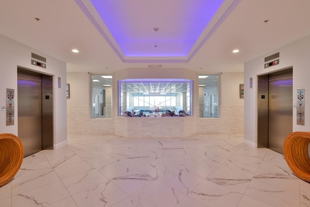 hallway with elevator, a tray ceiling, and tile walls