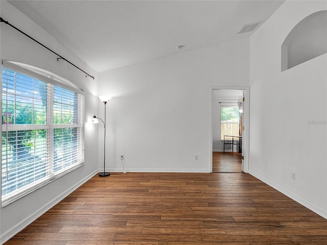 empty room with lofted ceiling, dark hardwood / wood-style floors, and a textured ceiling