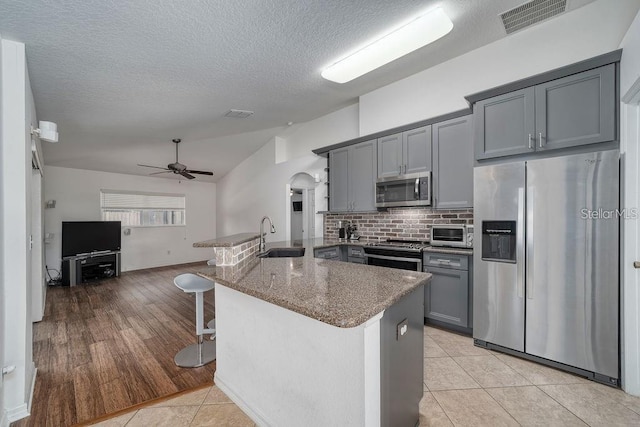 kitchen with sink, gray cabinets, appliances with stainless steel finishes, dark stone countertops, and a kitchen bar