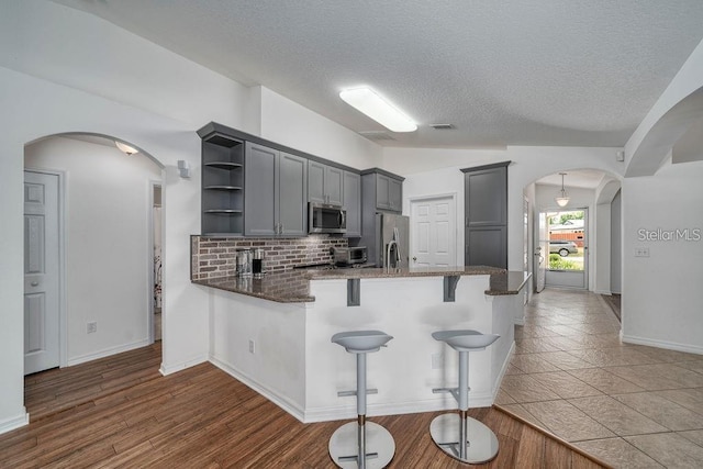 kitchen with vaulted ceiling, appliances with stainless steel finishes, gray cabinets, kitchen peninsula, and decorative backsplash