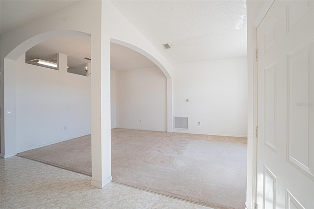 spare room with vaulted ceiling, light carpet, and a textured ceiling