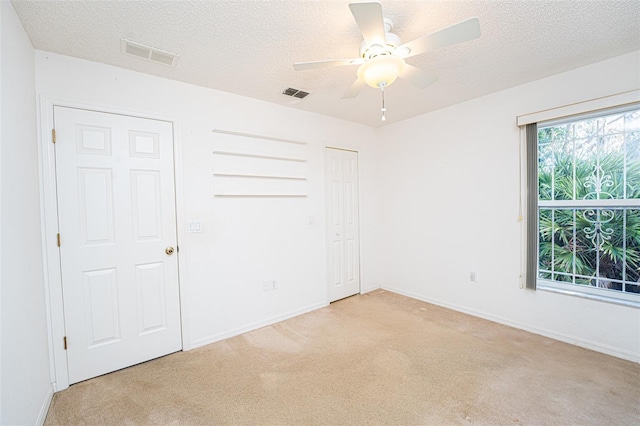 unfurnished bedroom featuring ceiling fan, light colored carpet, a closet, and a textured ceiling