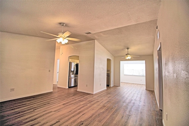 unfurnished living room with ceiling fan, vaulted ceiling, dark wood-type flooring, and a textured ceiling