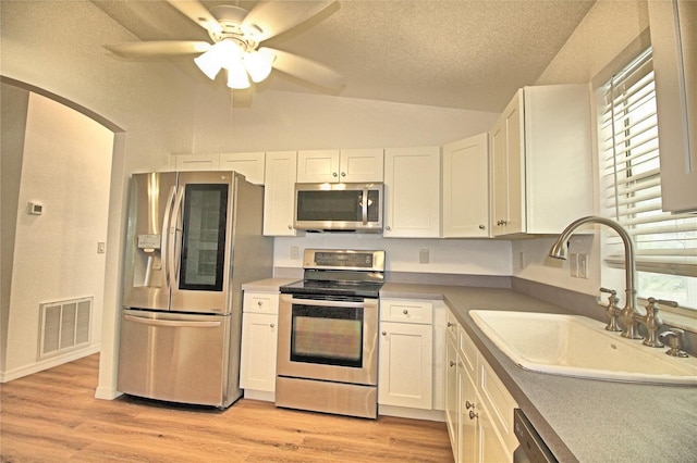 kitchen with lofted ceiling, sink, light hardwood / wood-style flooring, white cabinetry, and stainless steel appliances