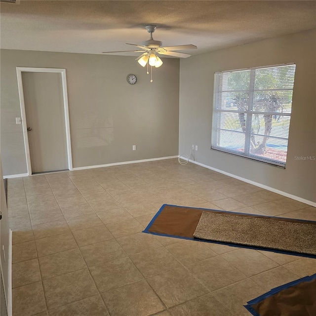 empty room with ceiling fan, a textured ceiling, and light tile patterned floors