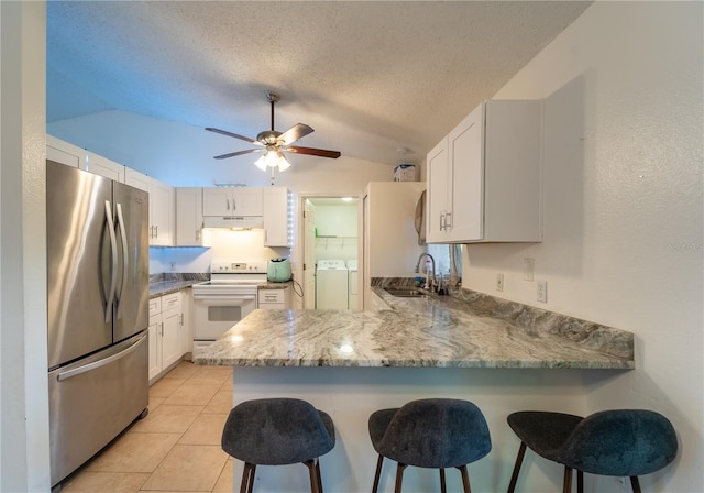 kitchen featuring washing machine and clothes dryer, white electric range oven, white cabinetry, stainless steel fridge, and kitchen peninsula