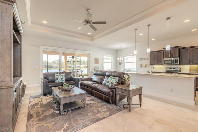 living room with a raised ceiling, ceiling fan with notable chandelier, a healthy amount of sunlight, and sink