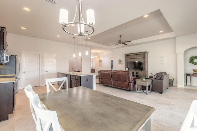 dining room featuring sink, a tray ceiling, ceiling fan with notable chandelier, and light tile patterned floors