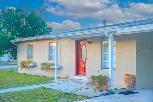 doorway to property with a lawn and stucco siding