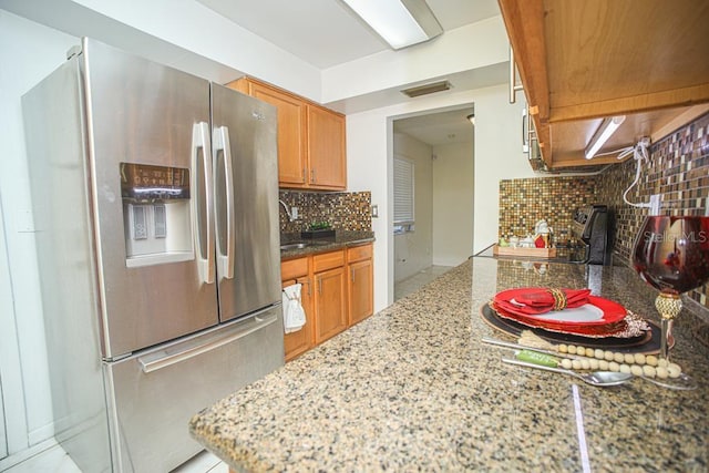 kitchen featuring light stone counters, range, backsplash, and stainless steel refrigerator with ice dispenser