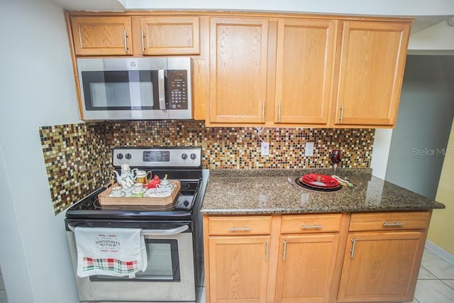 kitchen featuring backsplash, stainless steel appliances, light tile patterned floors, and dark stone countertops