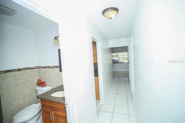 bathroom featuring tile walls, tile patterned flooring, vanity, toilet, and a textured ceiling