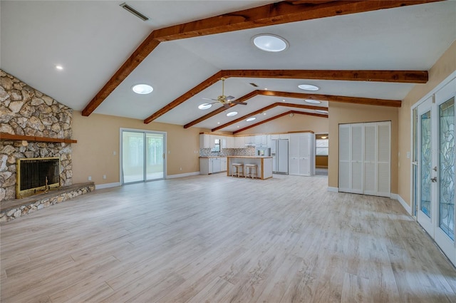 unfurnished living room with lofted ceiling with beams, ceiling fan, a fireplace, and light hardwood / wood-style floors