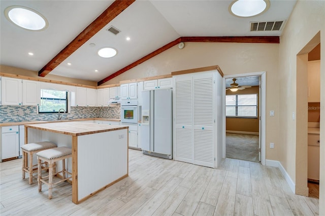 kitchen with white cabinetry, white refrigerator with ice dispenser, a kitchen breakfast bar, and a kitchen island