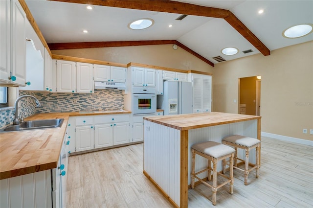 kitchen with white appliances, wooden counters, a center island, and white cabinets