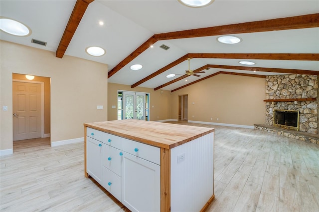 kitchen featuring wood counters, a stone fireplace, a center island, lofted ceiling with beams, and white cabinets