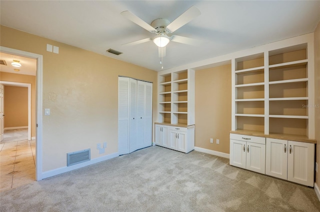 unfurnished living room with built in features, light colored carpet, and ceiling fan