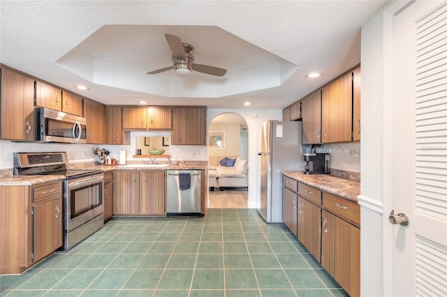 kitchen with stainless steel appliances, sink, backsplash, and a tray ceiling