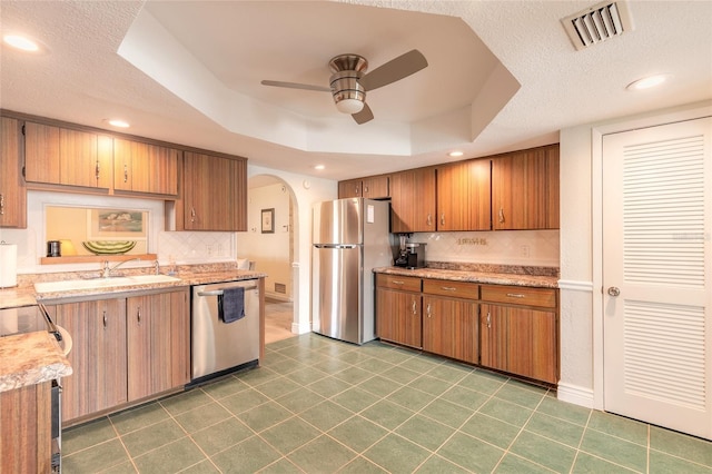 kitchen with appliances with stainless steel finishes, tasteful backsplash, dark tile patterned floors, ceiling fan, and a tray ceiling