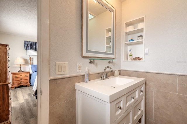 bathroom featuring hardwood / wood-style floors, tile walls, vanity, a textured ceiling, and built in shelves