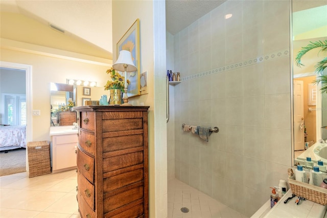 bathroom with tile patterned flooring, vanity, tiled shower, and a textured ceiling