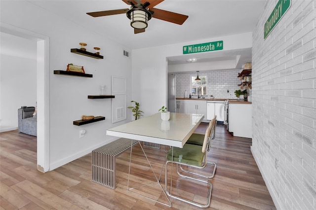 dining space featuring ceiling fan, brick wall, and light wood-type flooring