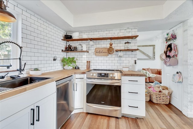 kitchen with white cabinetry, butcher block countertops, stainless steel appliances, and sink