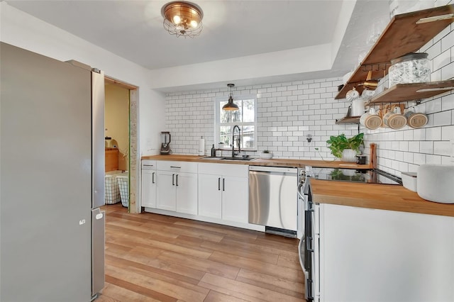 kitchen with decorative light fixtures, white cabinetry, butcher block counters, sink, and stainless steel appliances