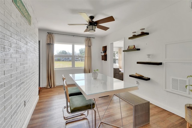 dining room with ceiling fan, brick wall, and light wood-type flooring