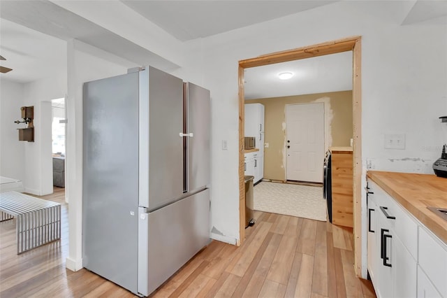 kitchen featuring ceiling fan, light hardwood / wood-style floors, stainless steel refrigerator, and white cabinets