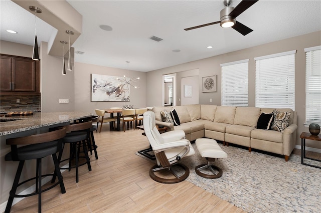 living room featuring ceiling fan with notable chandelier and light hardwood / wood-style floors