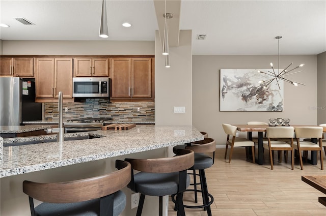 kitchen with pendant lighting, a breakfast bar, stainless steel appliances, tasteful backsplash, and light stone countertops