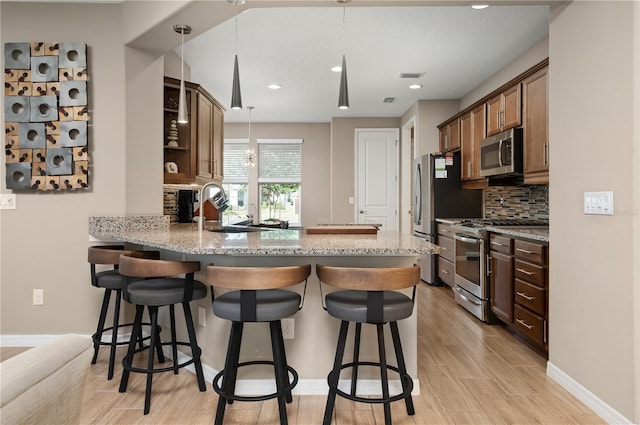 kitchen featuring appliances with stainless steel finishes, decorative backsplash, hanging light fixtures, light stone counters, and kitchen peninsula