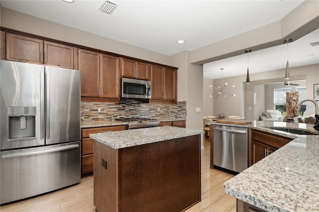 kitchen with sink, appliances with stainless steel finishes, light stone counters, a kitchen island, and decorative light fixtures