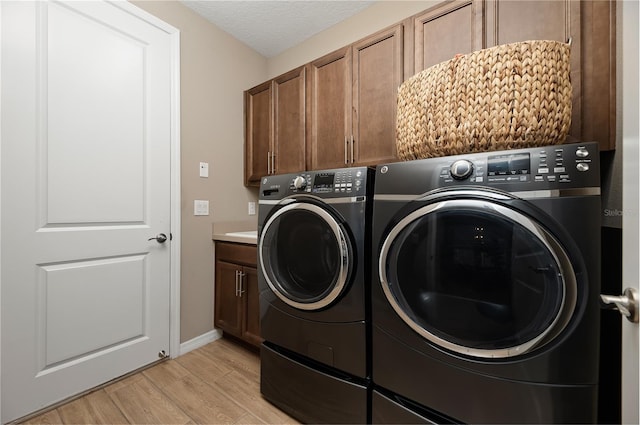 clothes washing area featuring separate washer and dryer, cabinets, a textured ceiling, and light wood-type flooring