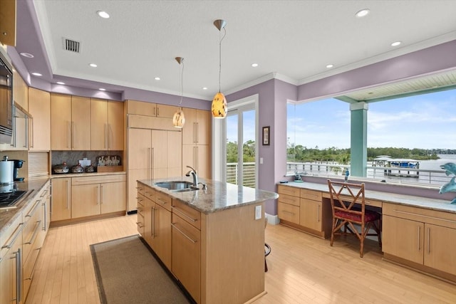 kitchen featuring light brown cabinetry, decorative light fixtures, sink, a kitchen island with sink, and a water view