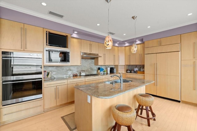 kitchen featuring built in appliances, sink, hanging light fixtures, and light brown cabinetry