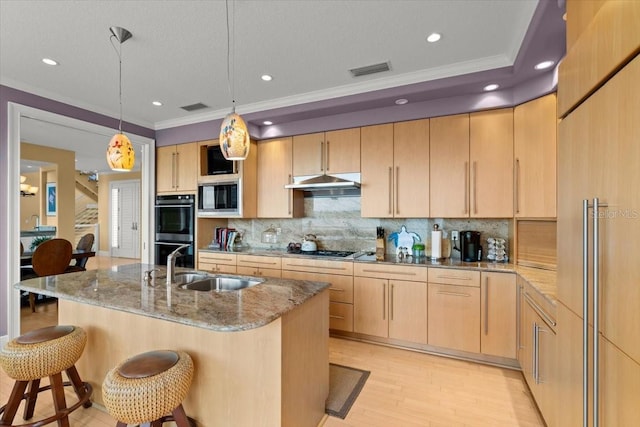 kitchen with stone countertops, pendant lighting, light brown cabinets, built in appliances, and a center island with sink