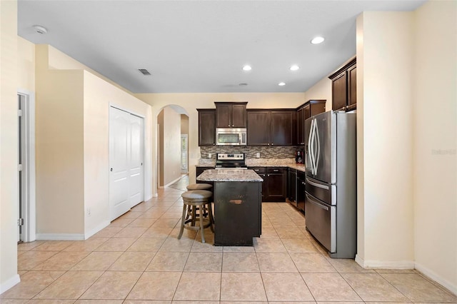 kitchen with a breakfast bar, dark brown cabinets, stainless steel appliances, a center island, and tasteful backsplash