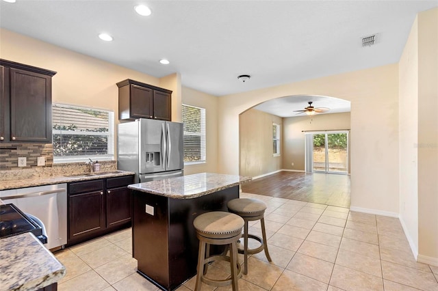 kitchen with dark brown cabinetry, a center island, stainless steel appliances, light stone countertops, and decorative backsplash