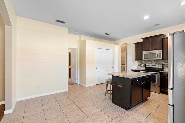 kitchen with a breakfast bar area, a center island, dark brown cabinets, stainless steel appliances, and decorative backsplash