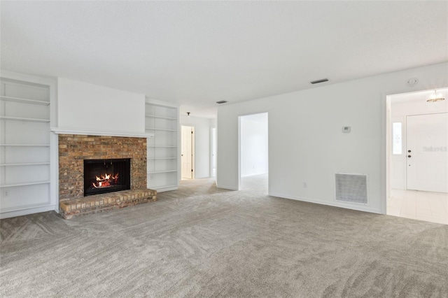 unfurnished living room with built in shelves, a brick fireplace, visible vents, and carpet flooring