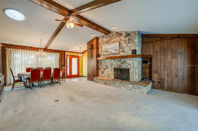 carpeted living room featuring vaulted ceiling with beams, a stone fireplace, ceiling fan with notable chandelier, and wood walls