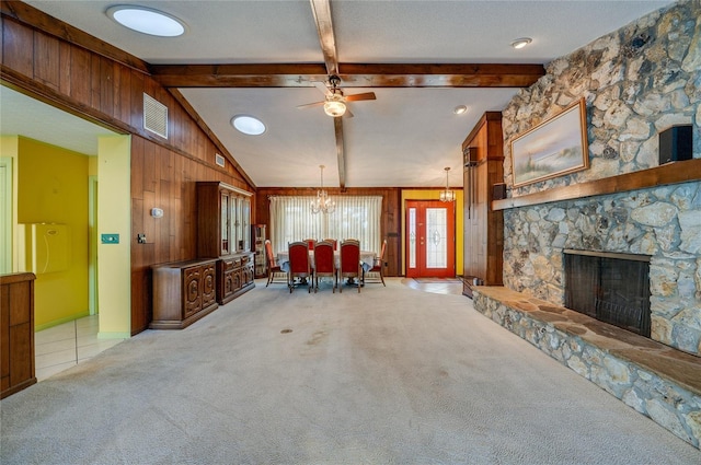 unfurnished living room featuring lofted ceiling with beams, light carpet, wooden walls, a fireplace, and ceiling fan with notable chandelier