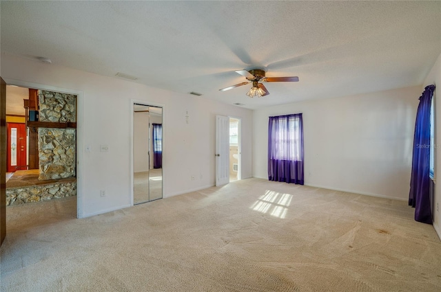 carpeted empty room featuring ceiling fan, a fireplace, and a textured ceiling