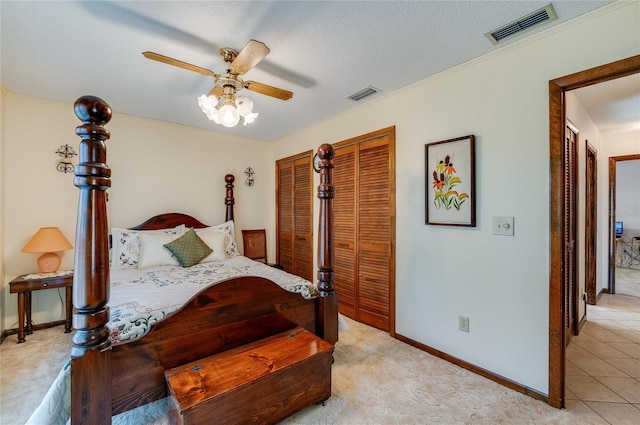 tiled bedroom featuring ceiling fan, two closets, and a textured ceiling